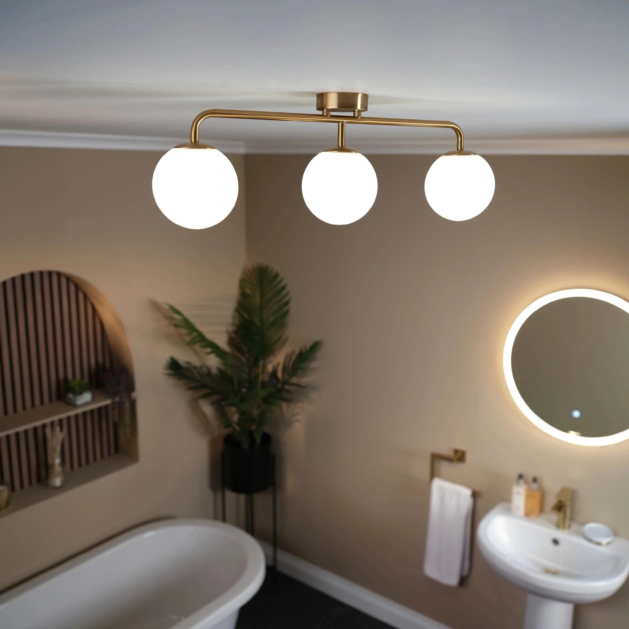 Solara 3 bar globe ceiling light in brass above a freestanding bath, with an illuminated round mirror